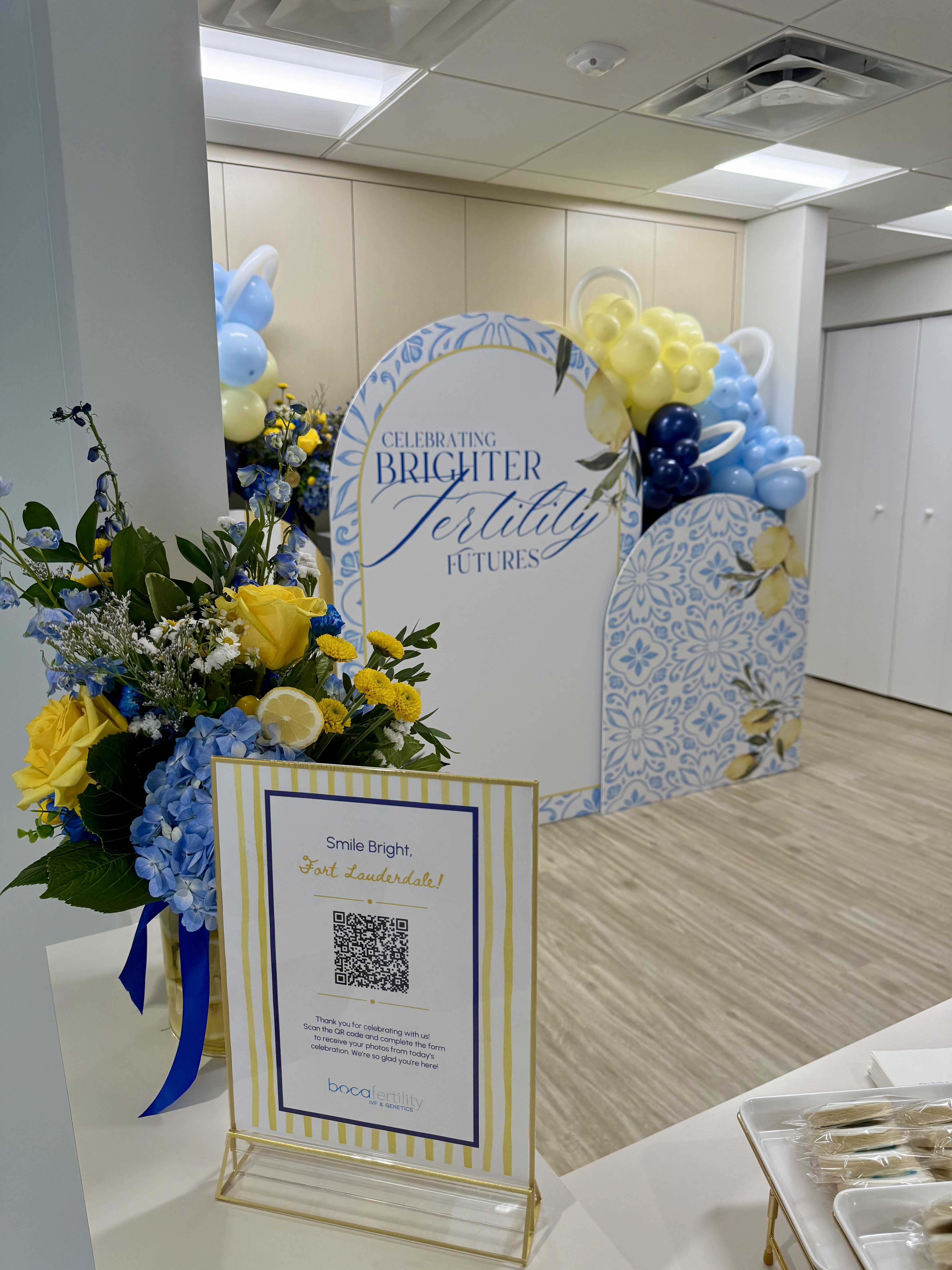 Corporate event backdrop with blue and yellow balloons and floral arrangements